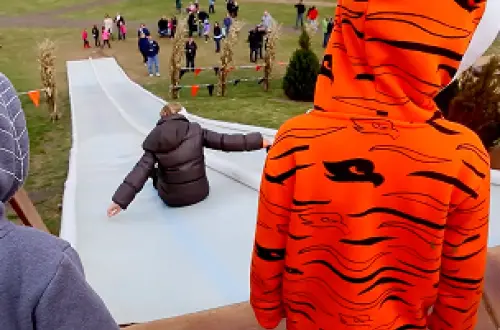 Un enfant vêtu d'un sweat à capuche orange et noir attend son tour pour descendre le toboggan. 
