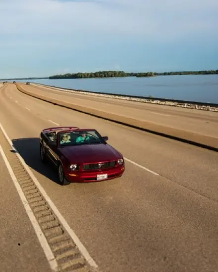 Une décapotable rouge roulant sur une route panoramique longeant le fleuve Mississippi.